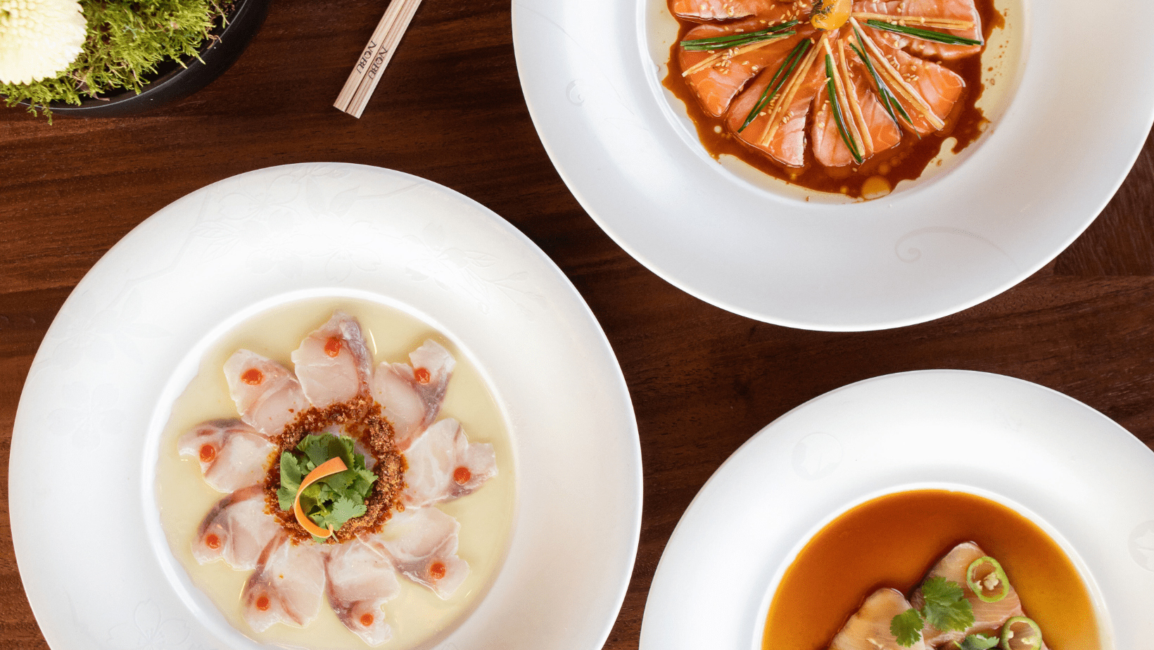 A wooden table displays three plates of food, showcasing a variety of colors and textures.