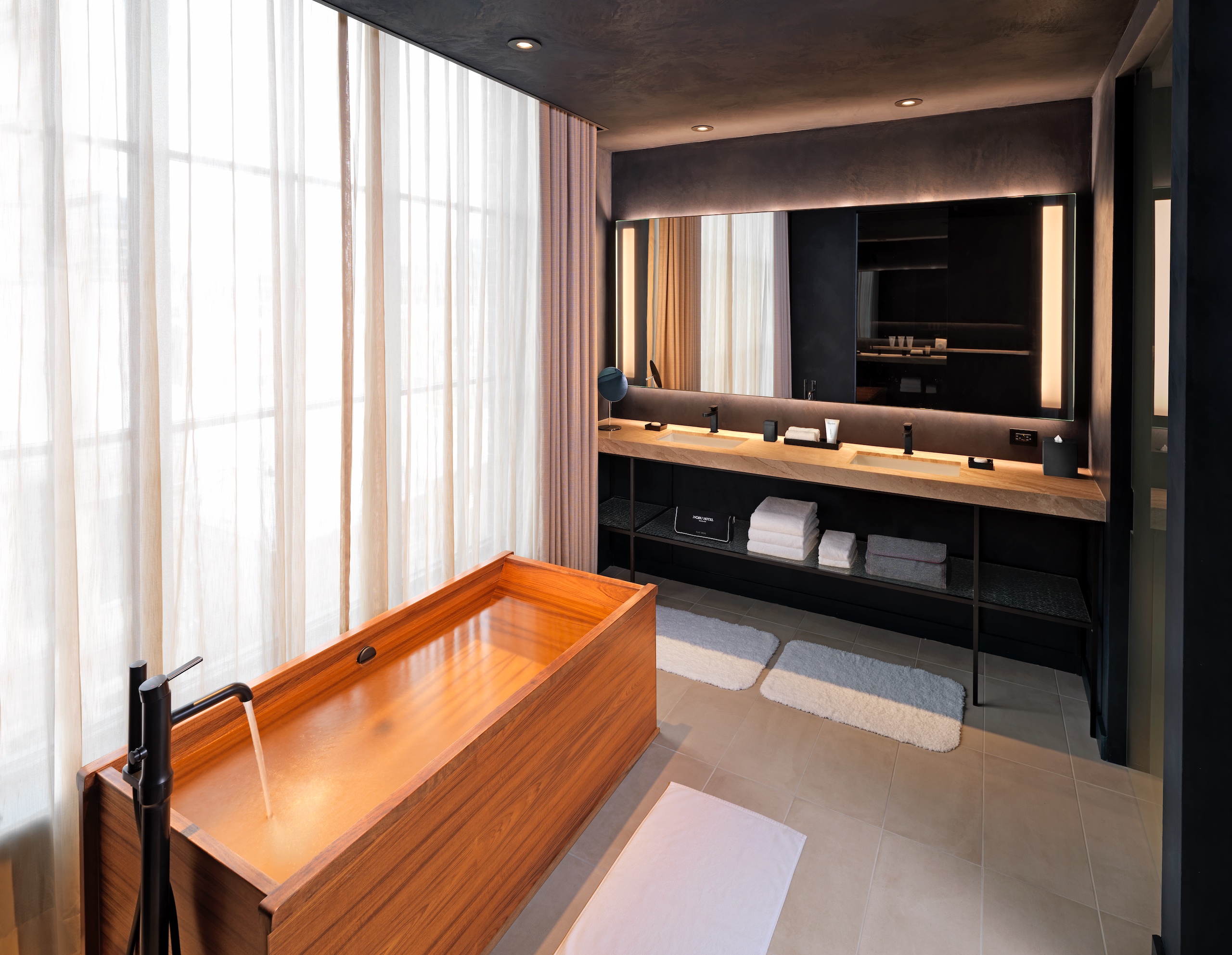dark bathroom with a wooden tub and large window with sheer curtains